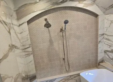 Arched marble shower with a patterned tile feature wall and a handheld showerhead