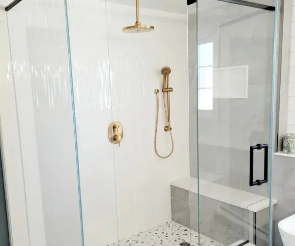 Walk-in shower with frameless glass, a brass rainfall showerhead and a tiled bench
