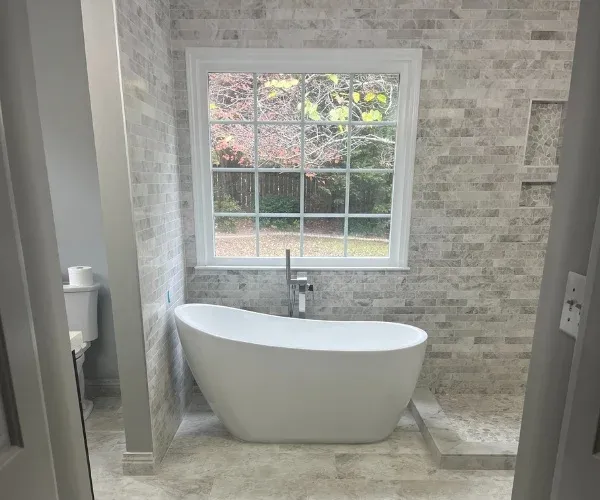 Freestanding soaking tub under a window with a stacked stone accent wall