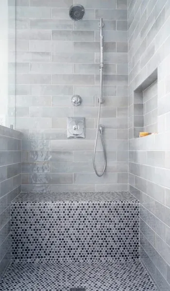 Gray tile walk-in shower with a mosaic floor and a recessed niche
