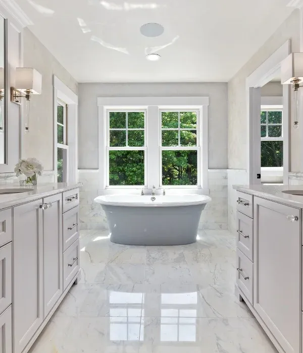 Bright bathroom renovation with two vanities and a freestanding tub between two windows