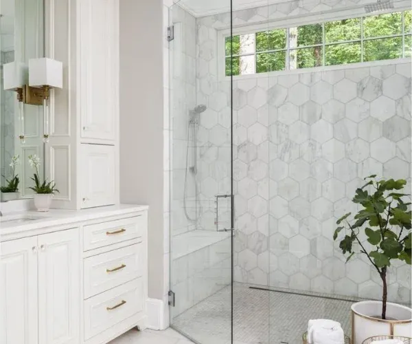 Frameless glass walk-in shower with marble hexagon tile next to a white vanity