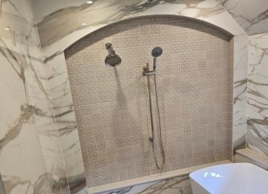 Luxury bathroom remodel in Wilmington, NC featuring a custom arched shower niche, marble tile walls, and dual showerheads.