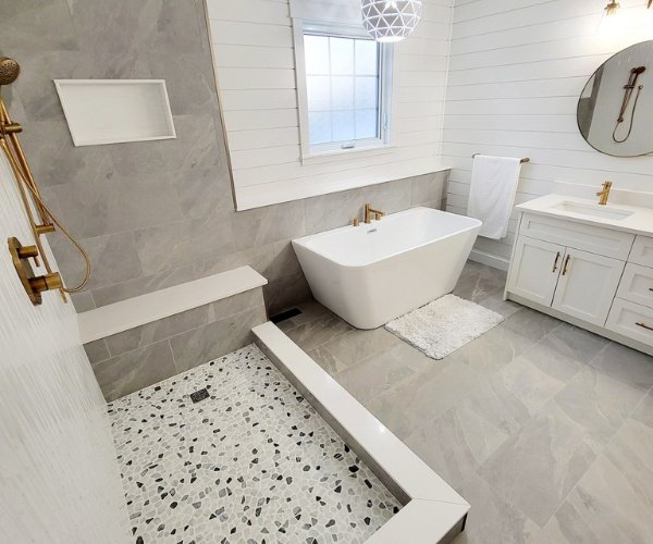 Bathroom remodel in Wilmington, NC featuring a freestanding tub, custom tile shower with a bench, gold fixtures, and modern shiplap walls.