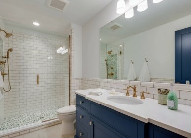 Bathroom remodeling project in Wilmington, NC featuring a blue vanity with gold fixtures, a glass-enclosed shower with subway tile, and a modern countertop design.